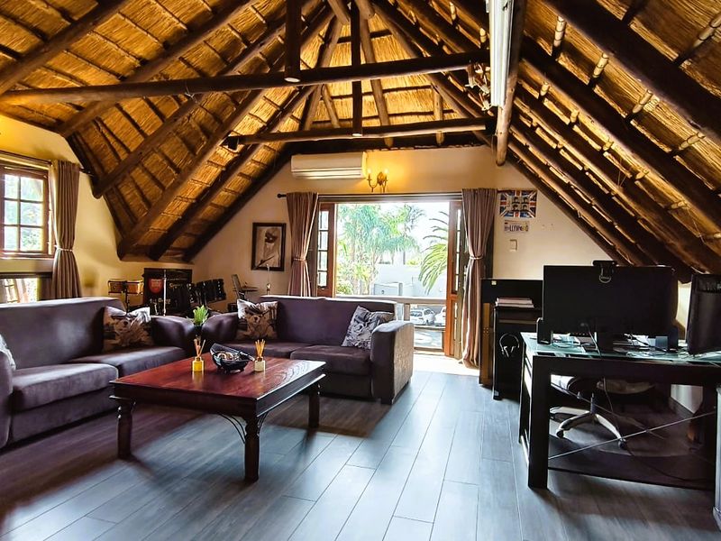 Spacious living area featuring a high vaulted thatched ceiling with exposed timber rafters, laminate flooring, and direct access to an outdoor space.