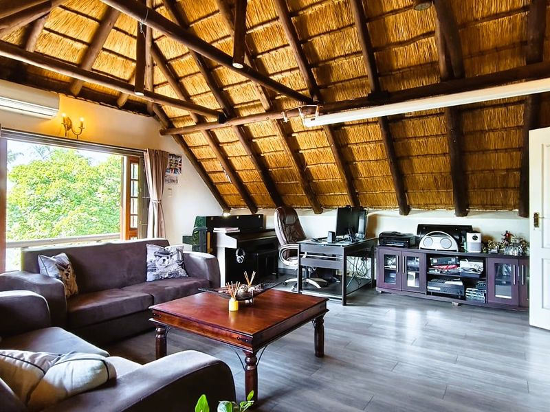 Spacious living area featuring a high vaulted ceiling with exposed timber rafters, traditional thatch roofing, and modern laminate flooring.