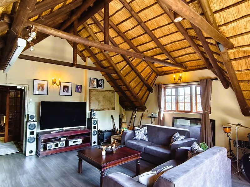 Spacious living room featuring a high vaulted ceiling with exposed timber trusses and traditional thatch roofing, complemented by modern laminate flooring.