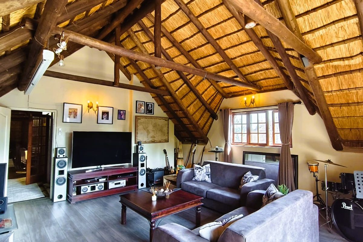 Spacious living room featuring a high vaulted ceiling with exposed timber trusses and traditional thatch roofing, complemented by modern laminate flooring.