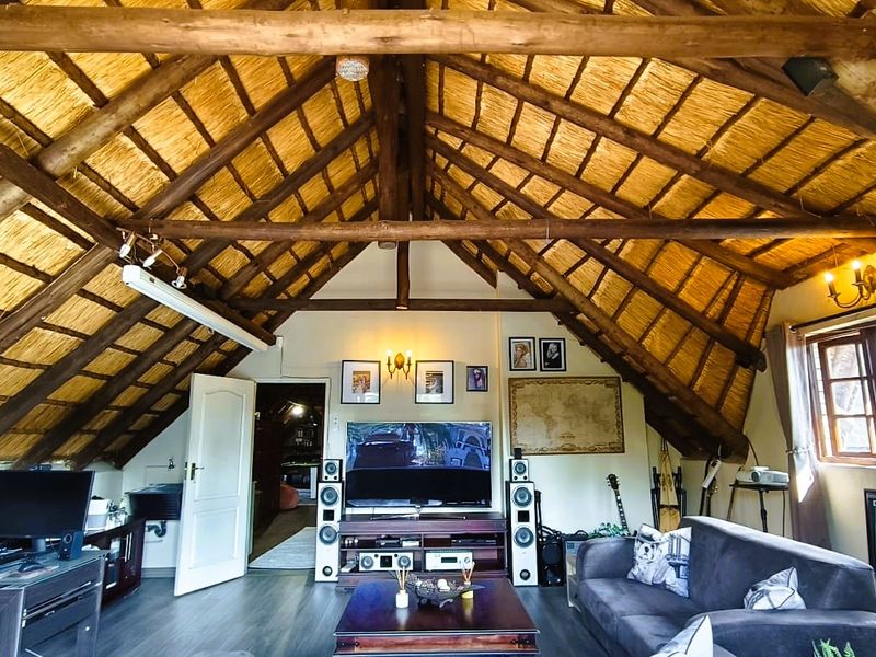 Spacious living area featuring a high vaulted ceiling with exposed timber rafters and traditional thatch roofing, complemented by modern laminate flooring.