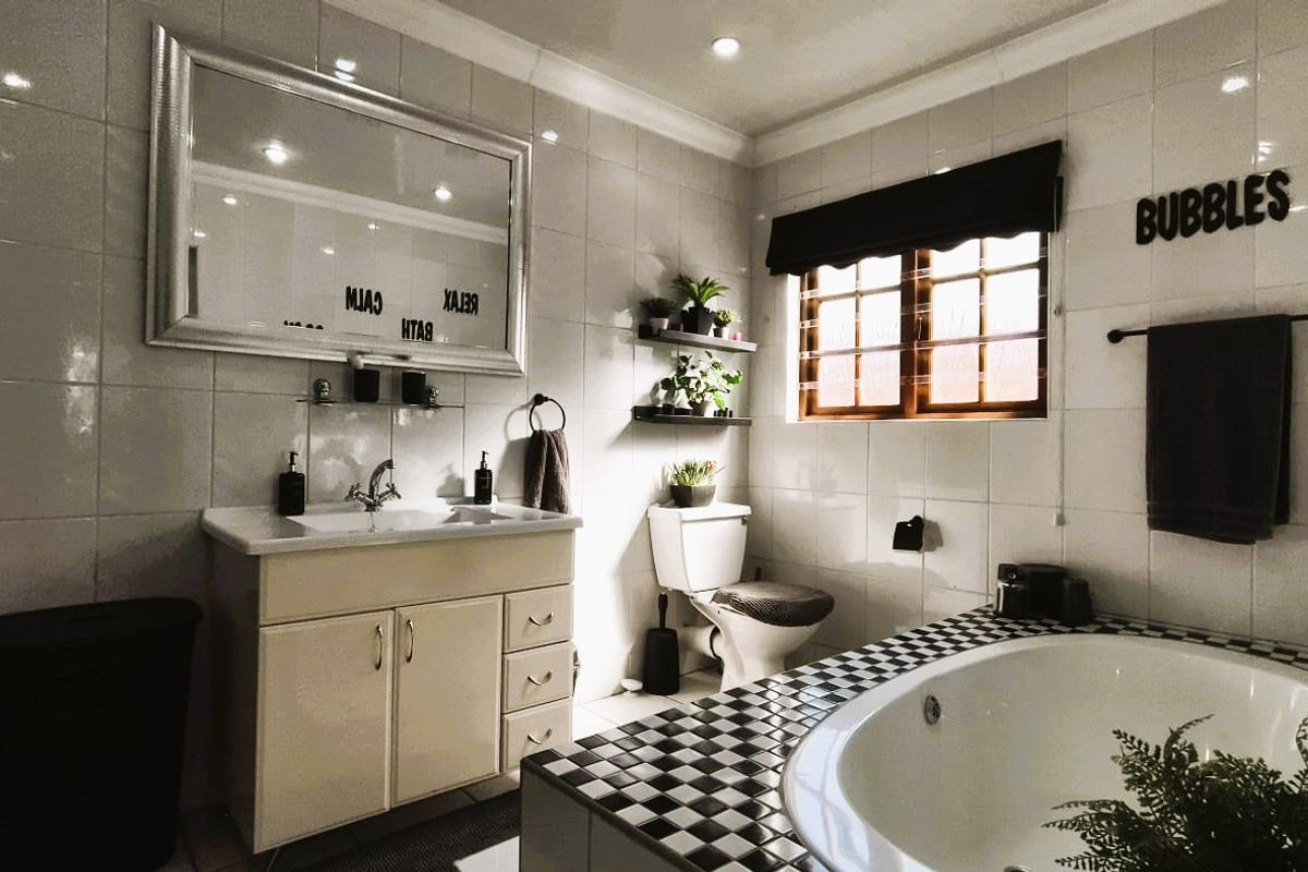 A well-lit bathroom featuring a vanity unit, a built-in bathtub with a checkerboard tile surround, and full-height wall tiling.