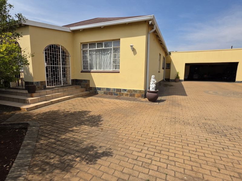 Front exterior view of the house featuring a paved driveway, attached garage, and tiled entrance steps with security gate.
