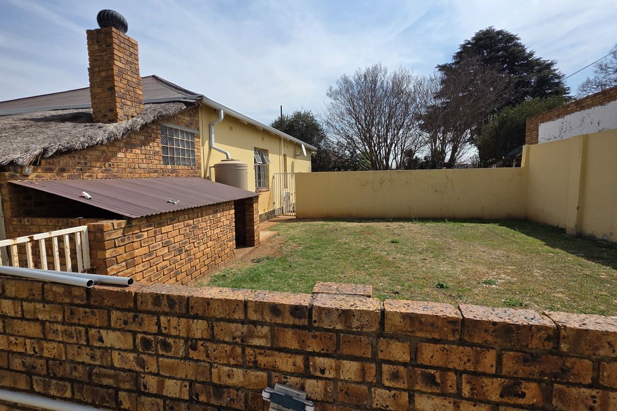 Rear exterior view of the property featuring a brick chimney, thatched roof section, and a private garden enclosed by brick boundary walls.