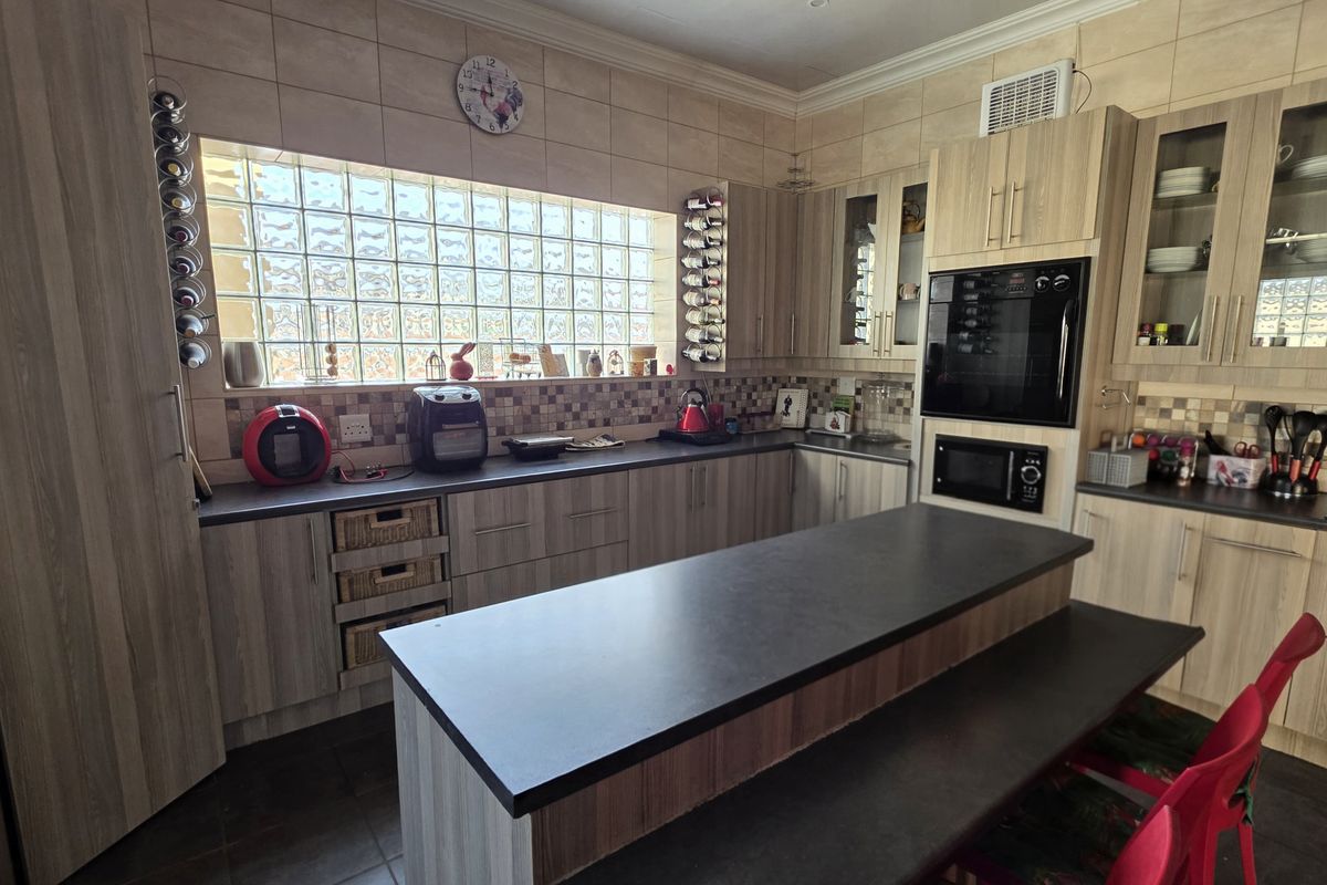 A functional kitchen featuring wood-look cabinetry, a central island with seating, built-in oven and microwave, and a distinctive glass block window.