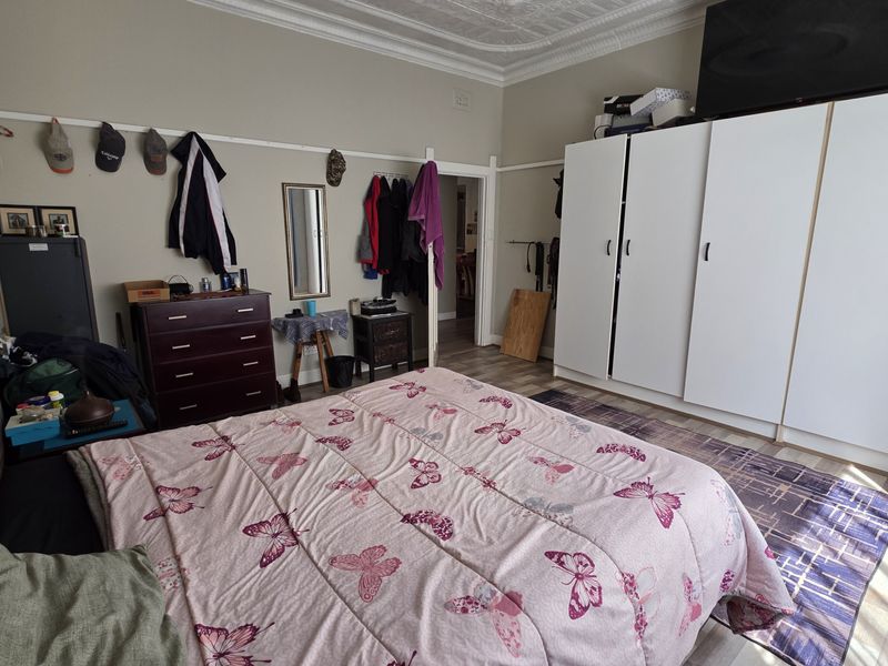 A spacious bedroom featuring built-in wardrobes, decorative ceiling detailing, and laminate flooring, offering a functional layout with ample storage space.