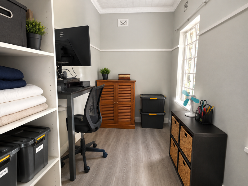 A functional home office space featuring light grey walls, laminate flooring, and classic grid-pattern windows, providing a bright and practical workspace.