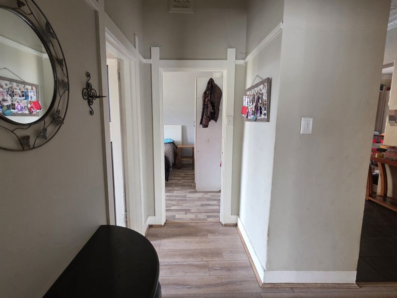 A narrow residential hallway featuring laminate flooring, traditional architraves, and decorative cornice, showing signs of wear on the walls and ceiling.