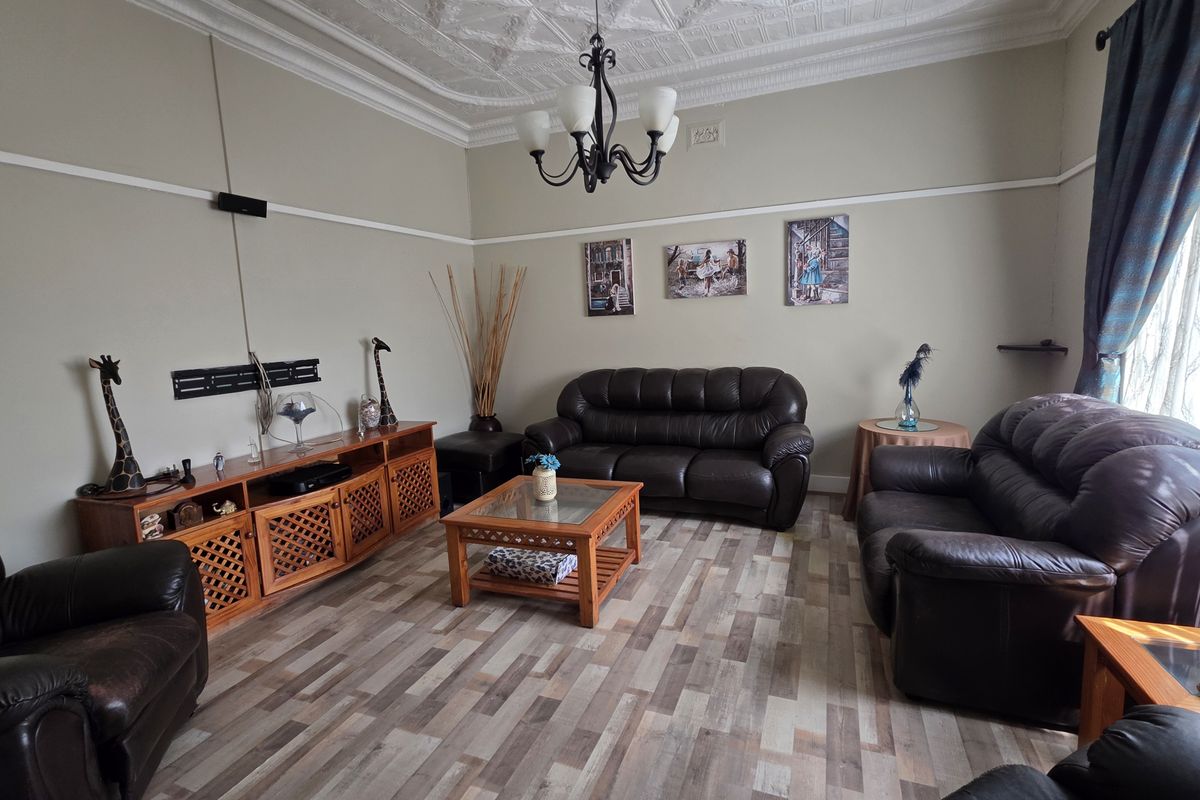 A spacious living room featuring an ornate pressed metal ceiling, classic picture rails, and modern laminate flooring, offering a blend of character and contemporary finishes.