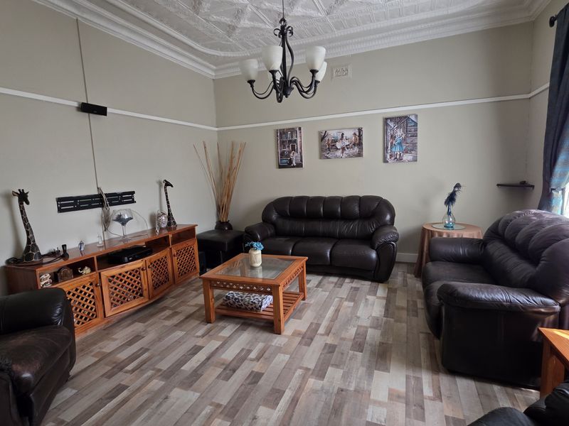 A spacious living room featuring an ornate pressed metal ceiling, classic picture rails, and modern laminate flooring, offering a blend of character and contemporary finishes.