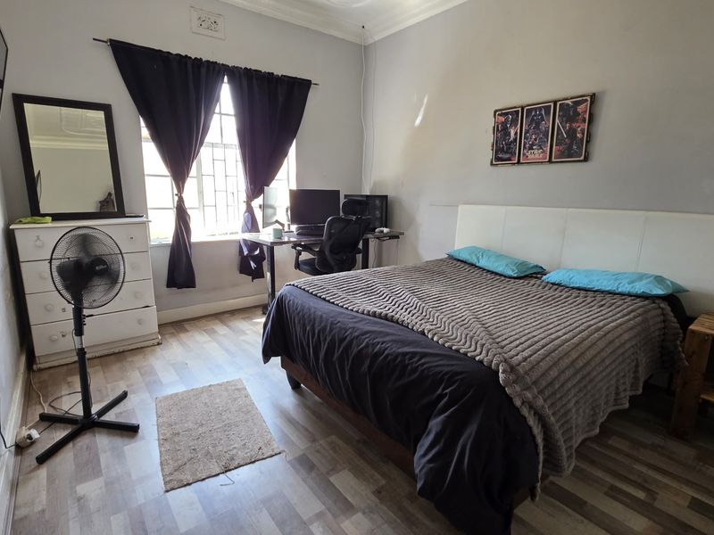 A functional bedroom featuring laminate flooring, a window with security bars, and decorative ceiling cornicing.