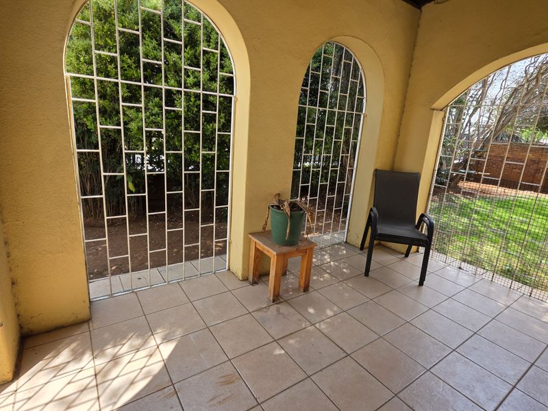 A covered patio area featuring tiled flooring and arched openings with security grilles, overlooking the rear garden.