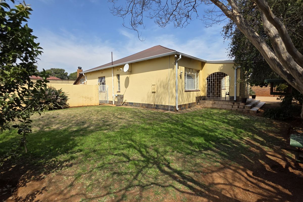 Rear view of the property featuring a spacious garden, covered patio area, and solid boundary walling.