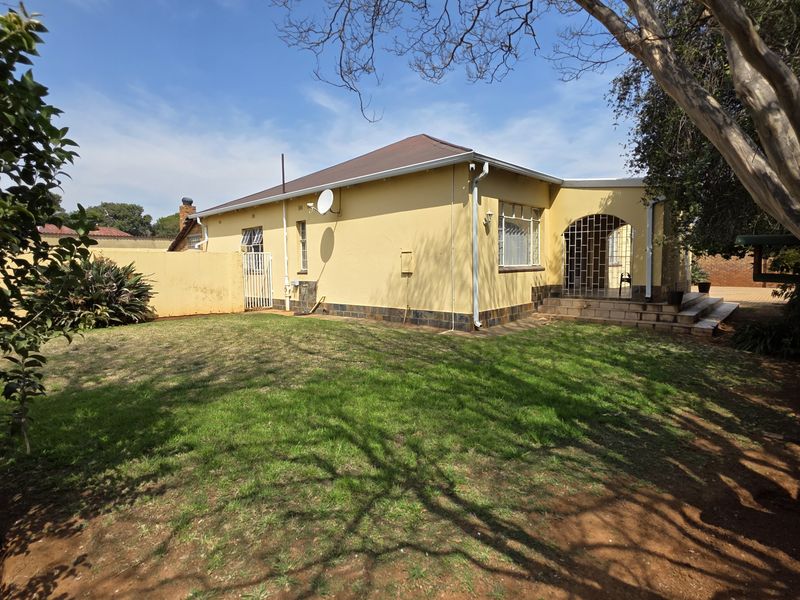 Rear view of the property featuring a spacious garden, covered patio area, and solid boundary walling.