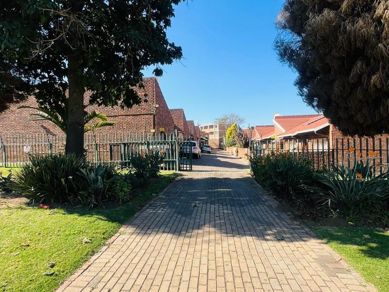 A view of the paved driveway leading into the residential complex, featuring brick-built units with tiled roofs and established perimeter fencing.