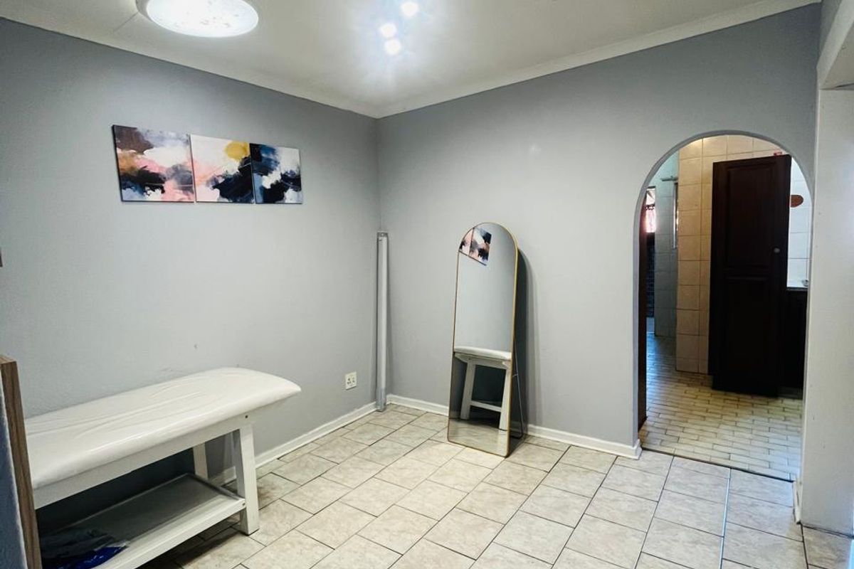 A neutral-toned room featuring tiled flooring and an arched entryway leading to an adjacent space, offering a clean and versatile layout.