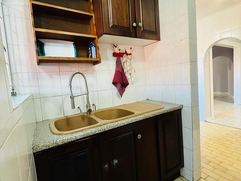 A functional scullery area featuring dark wood cabinetry, a double bowl sink with a gooseneck faucet, and tiled wall and floor finishes.