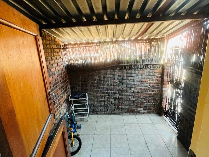 A covered outdoor patio area featuring exposed brick walls, tiled flooring, and a utility sink, providing a functional space for laundry or outdoor storage.