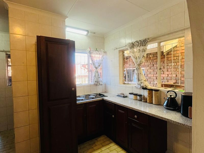 A compact kitchen featuring dark wood cabinetry, laminate countertops, an integrated electric hob, and tiled finishes throughout.