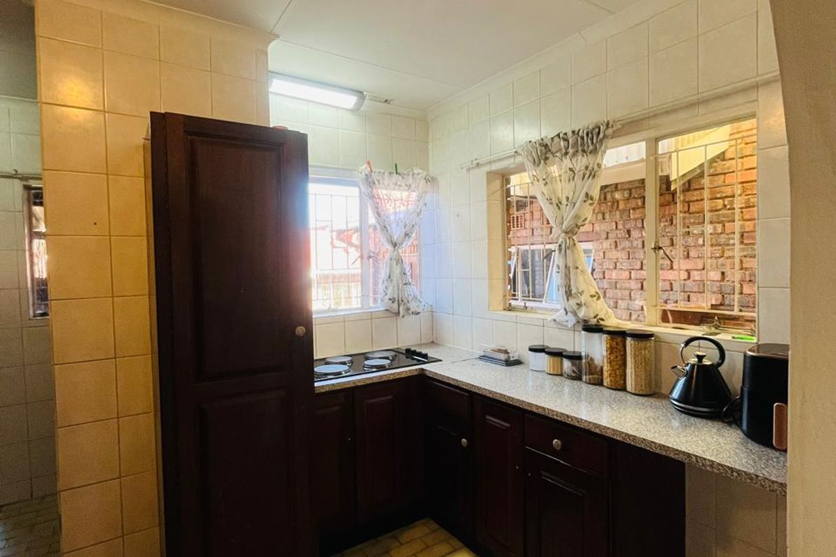 A compact kitchen featuring dark wood cabinetry, laminate countertops, an integrated electric hob, and tiled finishes throughout.