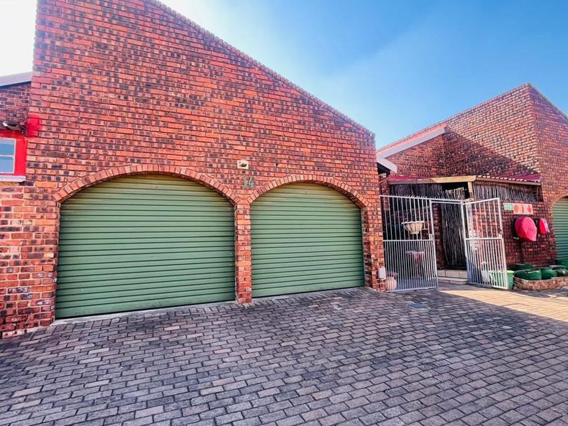 A double garage featuring face brick construction, green roller doors, and a paved driveway entrance.