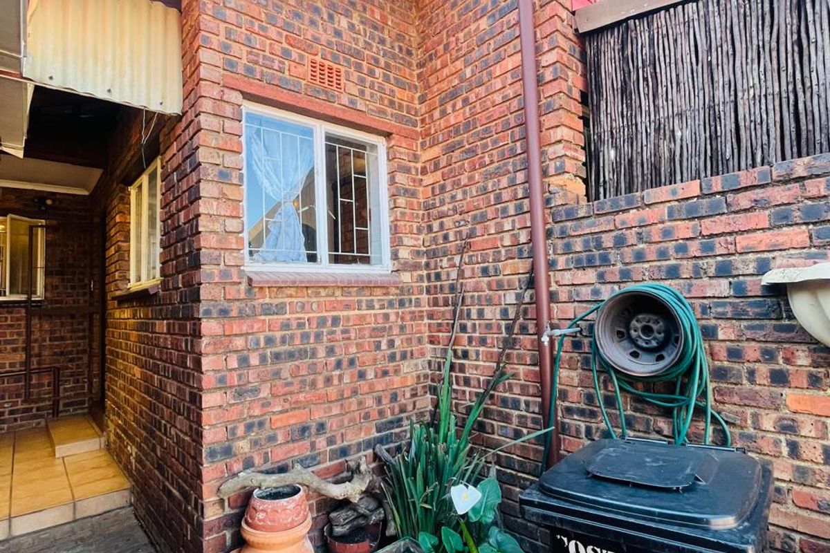 A view of the rear exterior area featuring face brick walls, a paved walkway, and a functional downpipe system.
