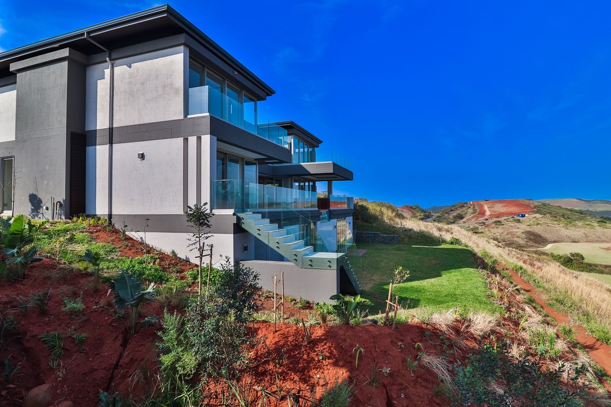Modern multi-level residence featuring glass balustrades, expansive balconies, and a landscaped rear garden with scenic hillside views.