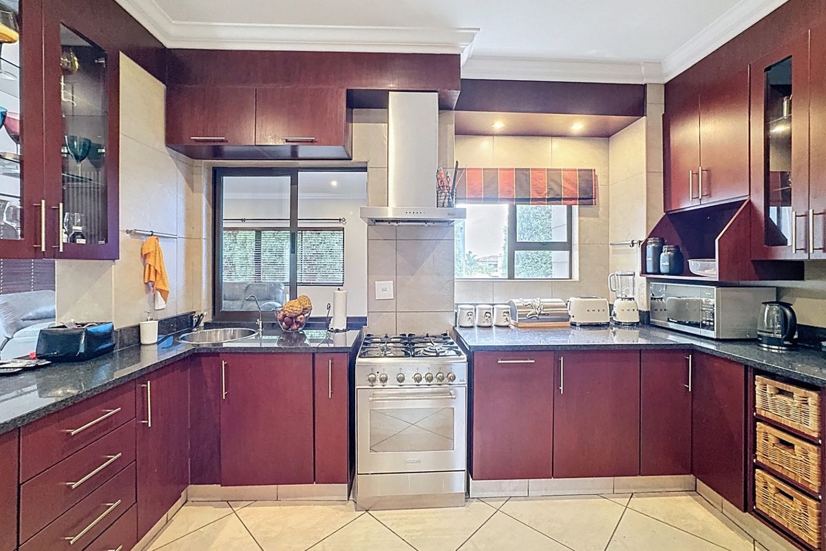 A well-maintained kitchen featuring dark wood cabinetry, granite countertops, a stainless steel gas stove with extractor fan, and tiled flooring.