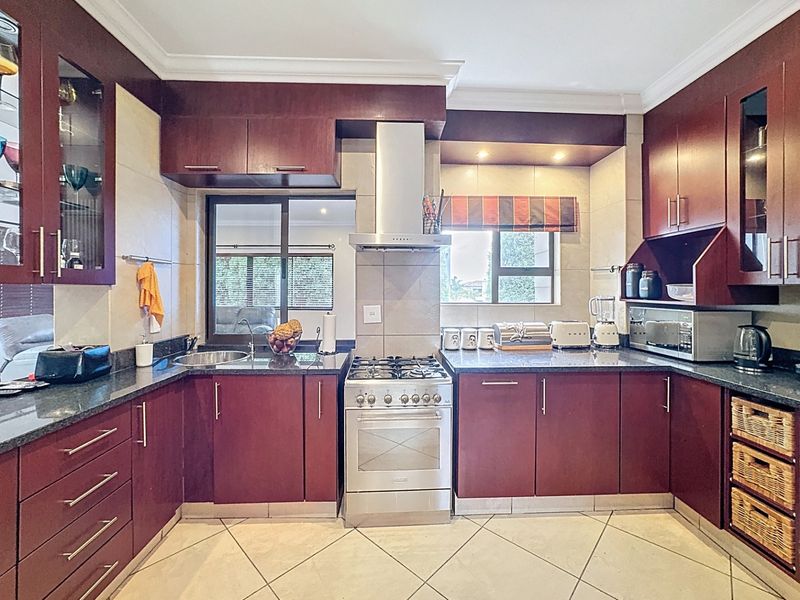 A well-maintained kitchen featuring dark wood cabinetry, granite countertops, a stainless steel gas stove with extractor fan, and tiled flooring.
