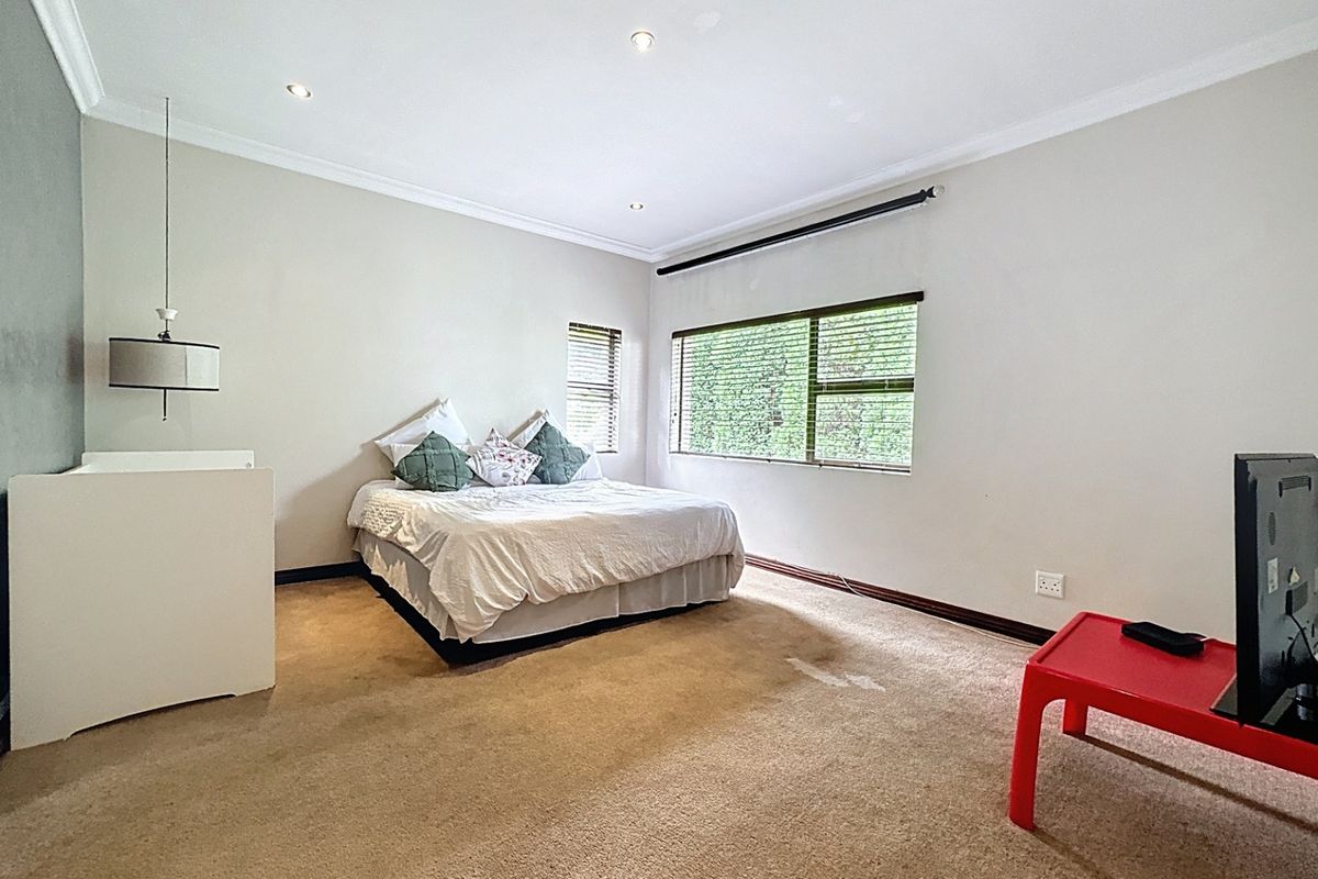 A spacious bedroom featuring neutral walls, carpeted flooring, recessed downlighting, and large windows with fitted venetian blinds.