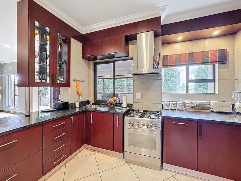 A well-maintained kitchen featuring dark wood cabinetry, granite countertops, a stainless steel gas stove with extractor fan, and tiled flooring.