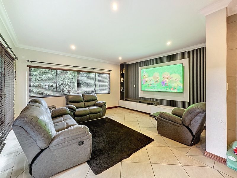 Spacious living room featuring a modern built-in media wall with slatted feature paneling, recessed downlights, and neutral tiled flooring.