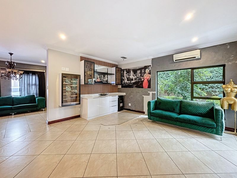 Spacious living area featuring tiled floors, a built-in bar unit, and large windows providing natural light and garden views.