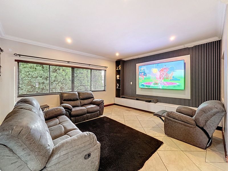 Spacious living room featuring a modern slatted feature wall with built-in media console, recessed downlights, and tiled flooring.