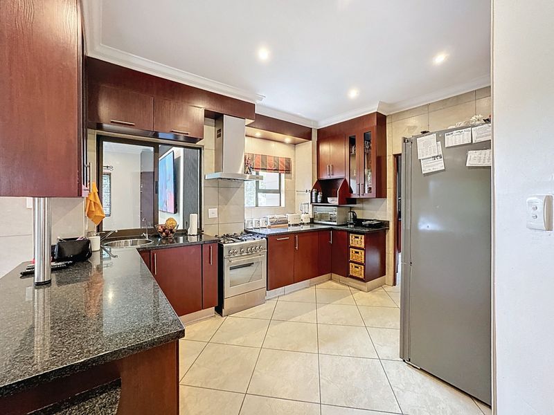 A functional kitchen featuring dark wood cabinetry, granite countertops, stainless steel appliances, and tiled flooring with ample storage space.