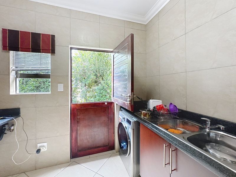 A functional laundry area featuring tiled walls, granite countertops, double stainless steel sink, and a stable door providing direct outdoor access.