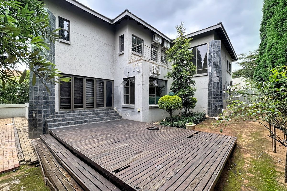 Rear view of a two-story house featuring a large timber deck, stone-clad pillars, and an upper-level balcony with air conditioning units.