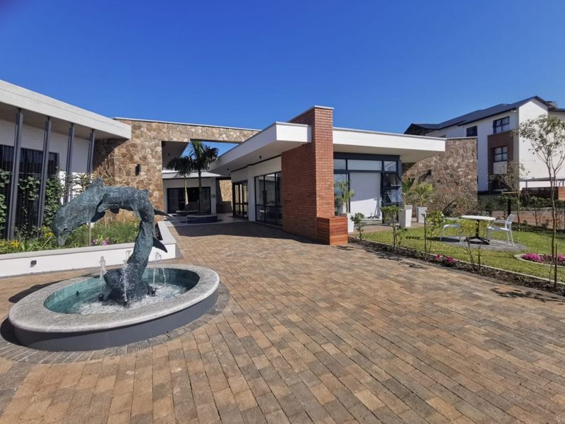 A modern clubhouse exterior featuring stone and brick architectural elements, a central water feature, and a well-maintained paved courtyard area.