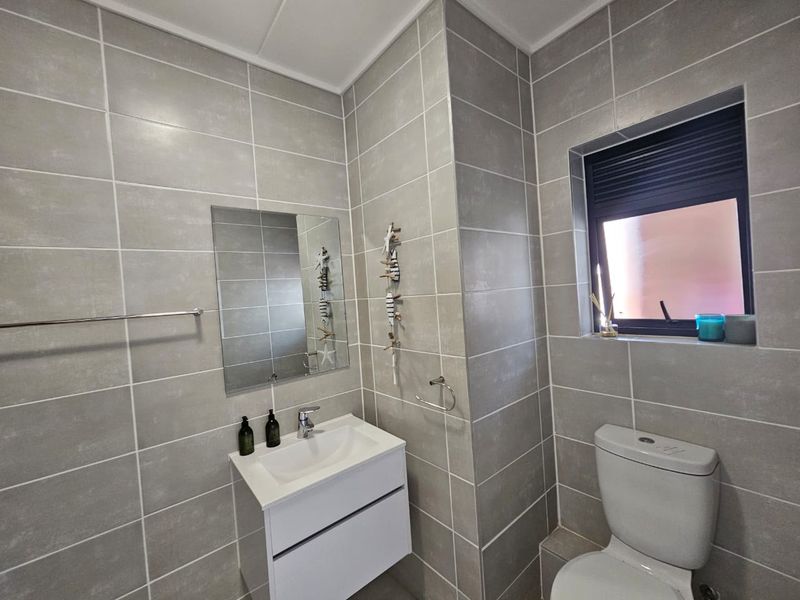 Modern bathroom featuring grey wall tiles, a wall-mounted vanity with a basin, and a toilet.