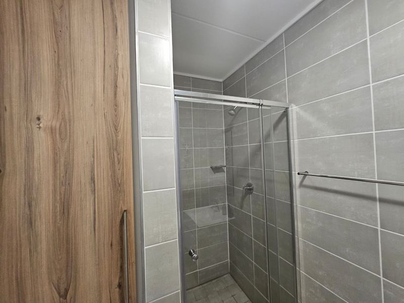 A modern bathroom featuring a glass-enclosed shower with grey ceramic wall tiles and wood-look built-in cabinetry.