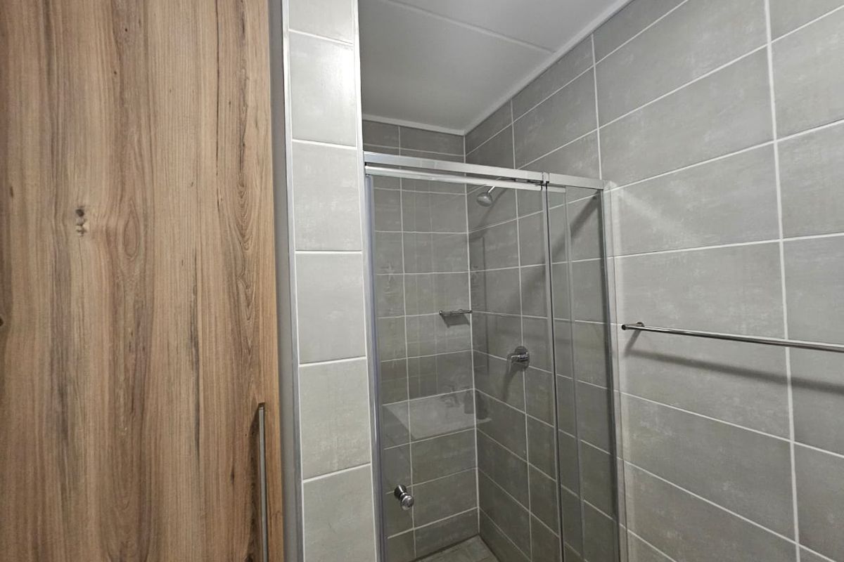 A modern bathroom featuring a glass-enclosed shower with grey ceramic wall tiles and wood-look built-in cabinetry.