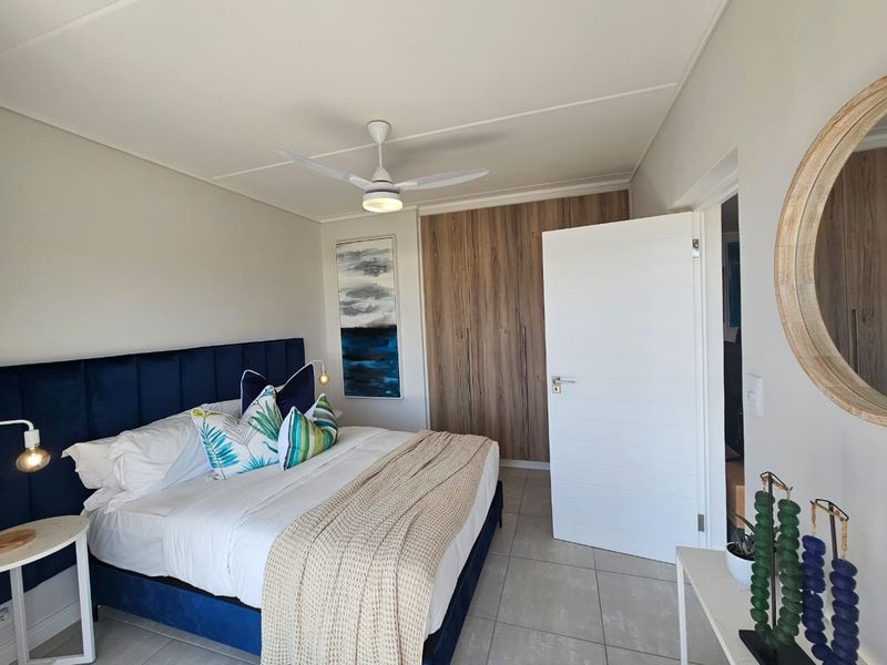A well-maintained bedroom featuring neutral tiled flooring, built-in wooden cupboards, and a modern ceiling fan.