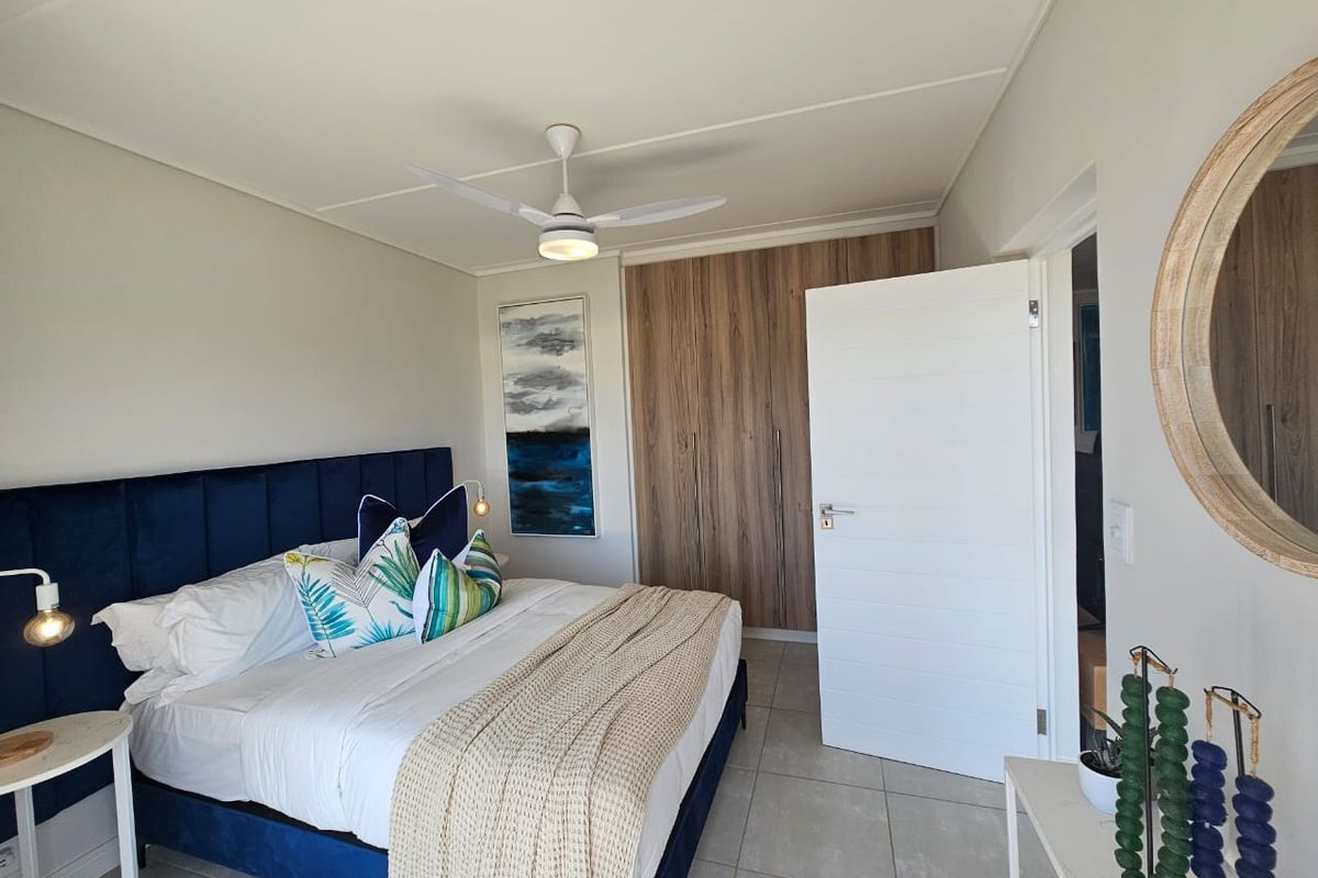 A well-maintained bedroom featuring neutral tiled flooring, built-in wooden cupboards, and a modern ceiling fan.