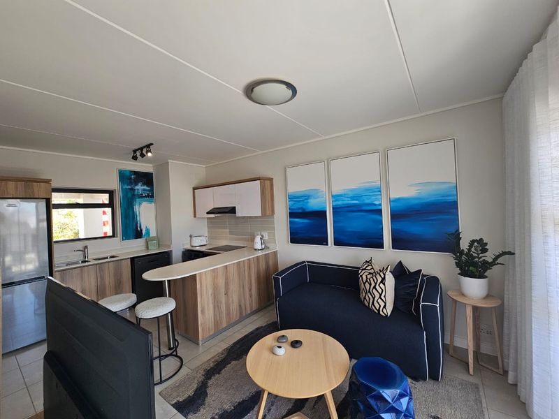 A modern open-plan living area featuring a compact kitchen with wood-finish cabinetry, a breakfast bar, and tiled flooring throughout.