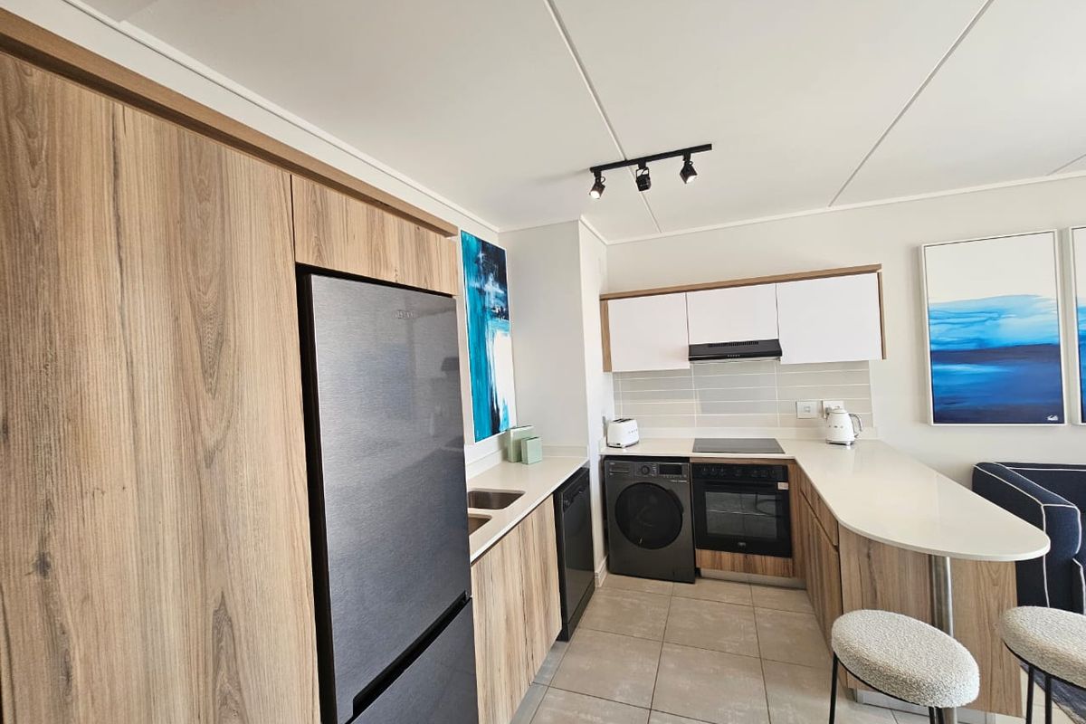 Modern kitchen featuring wood-grain cabinetry, stone countertops, integrated oven, electric hob, and a breakfast bar, finished with neutral tiled flooring.