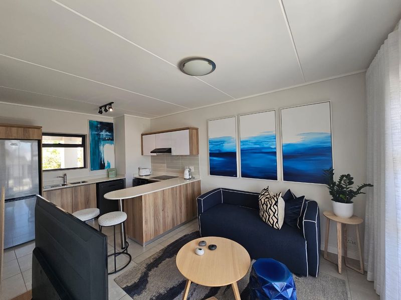 Modern open-plan living area featuring a compact kitchen with wood-finish cabinetry, breakfast bar, and tiled flooring, seamlessly integrated with the lounge space.
