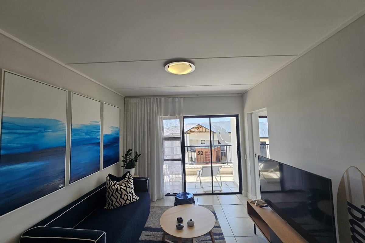 A bright living room featuring tiled flooring and a sliding glass door that provides access to an outdoor balcony area.