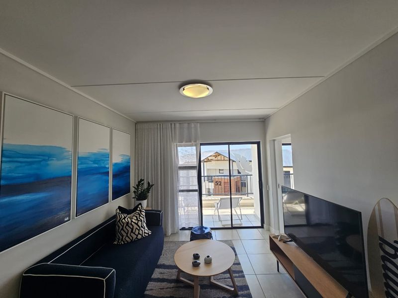 A bright living room featuring tiled flooring and a sliding glass door that provides access to an outdoor balcony area.