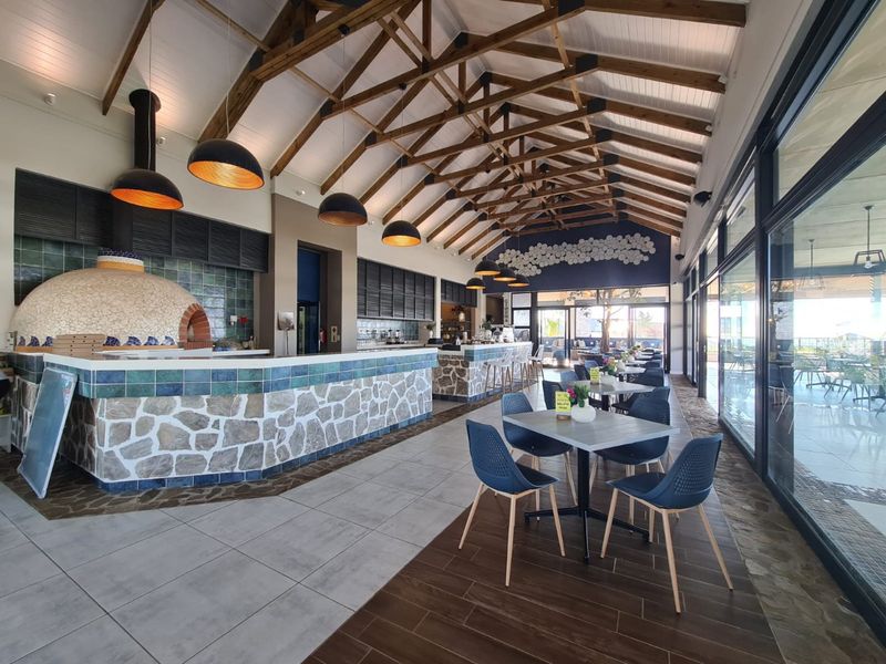 Spacious open-plan dining area featuring a vaulted ceiling with exposed timber trusses, a stone-clad service counter, built-in pizza oven, and expansive glass sliding doors.