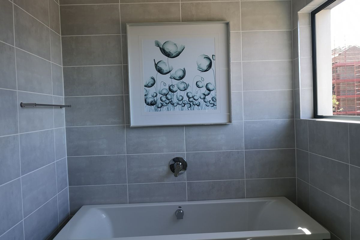 A modern bathroom featuring a built-in bathtub with wall-mounted chrome fixtures and neutral grey ceramic wall tiles.